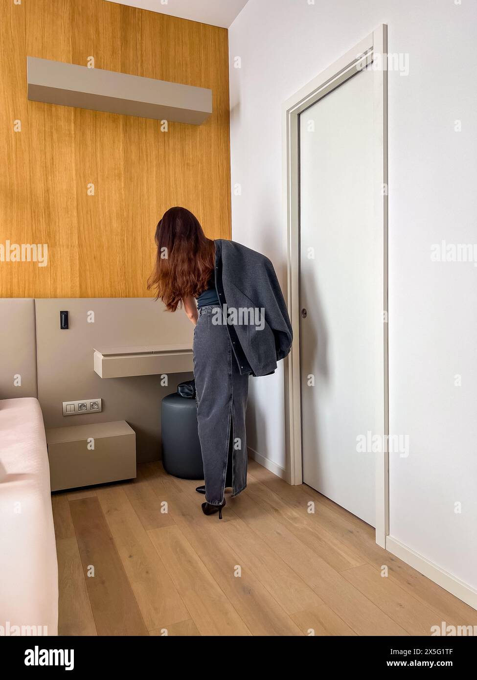 Une jeune femme élancée se tient près d'une table de boudoir, portant une jupe maxi en denim. Vue de l'arrière Banque D'Images