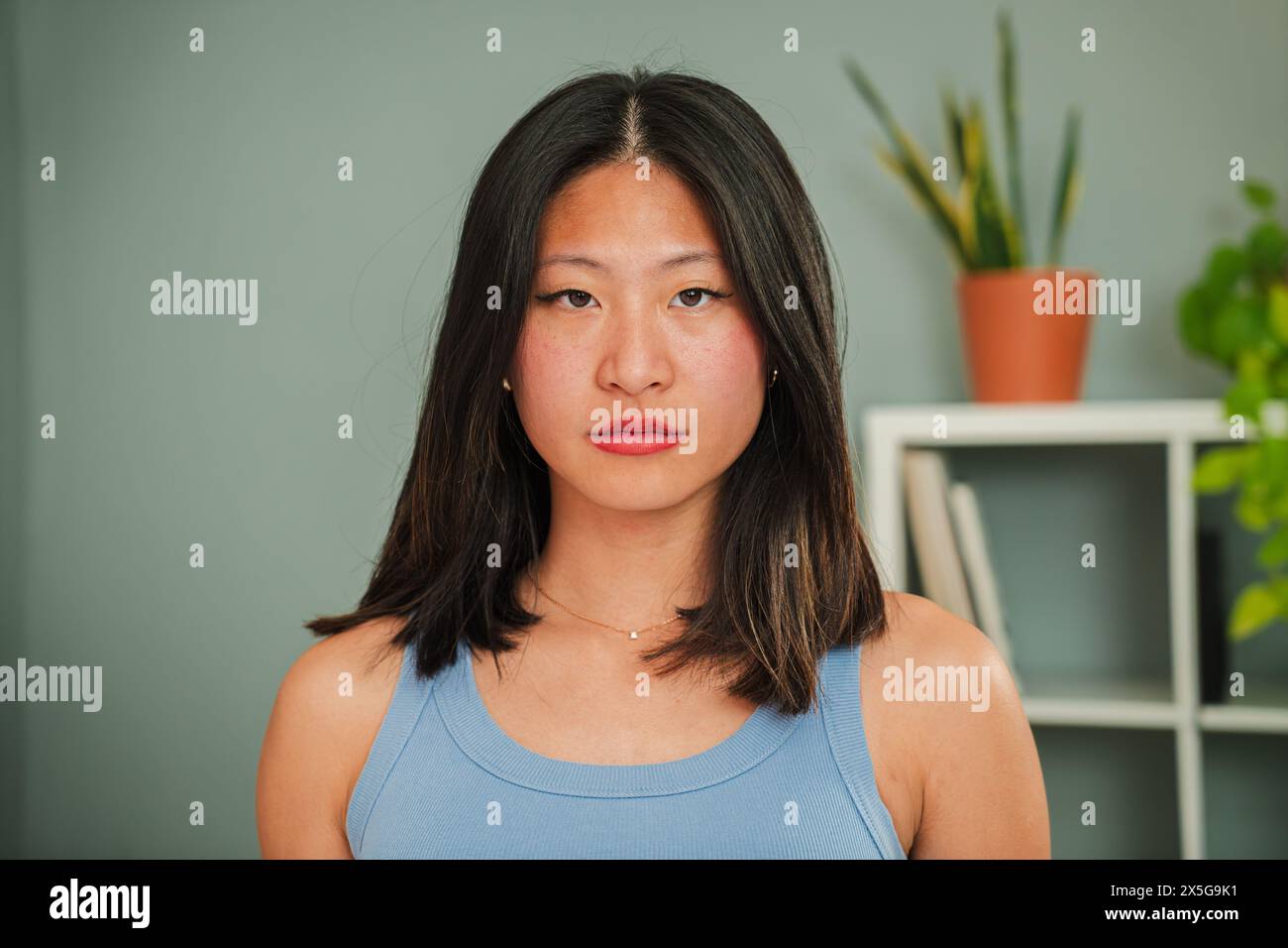 Gros plan portrait individuel d'une jeune femme asiatique sérieuse regardant la caméra debout à la maison Linving Room. Une femme chinoise penghtufl avec l'expression confiante, pensive et sombre vraie fille froncant les sourcils. Photo de haute qualité Banque D'Images