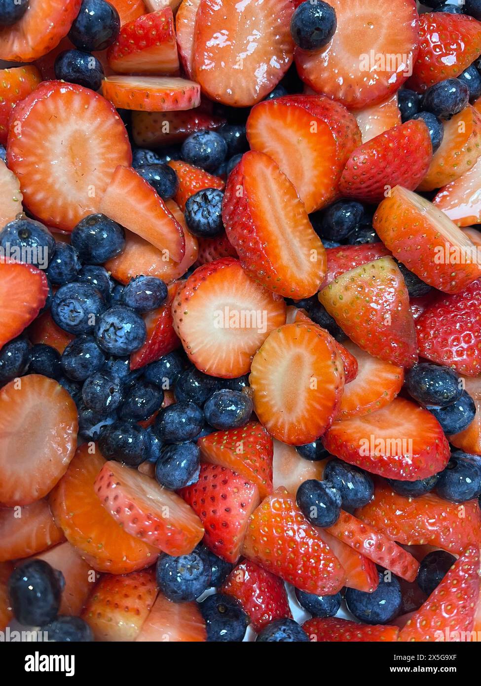 Une vue rapprochée de fraises mûres et de bleuets soigneusement disposés sur une assiette blanche. Les fraises rouges contrastent avec les bleuets, créant un Banque D'Images