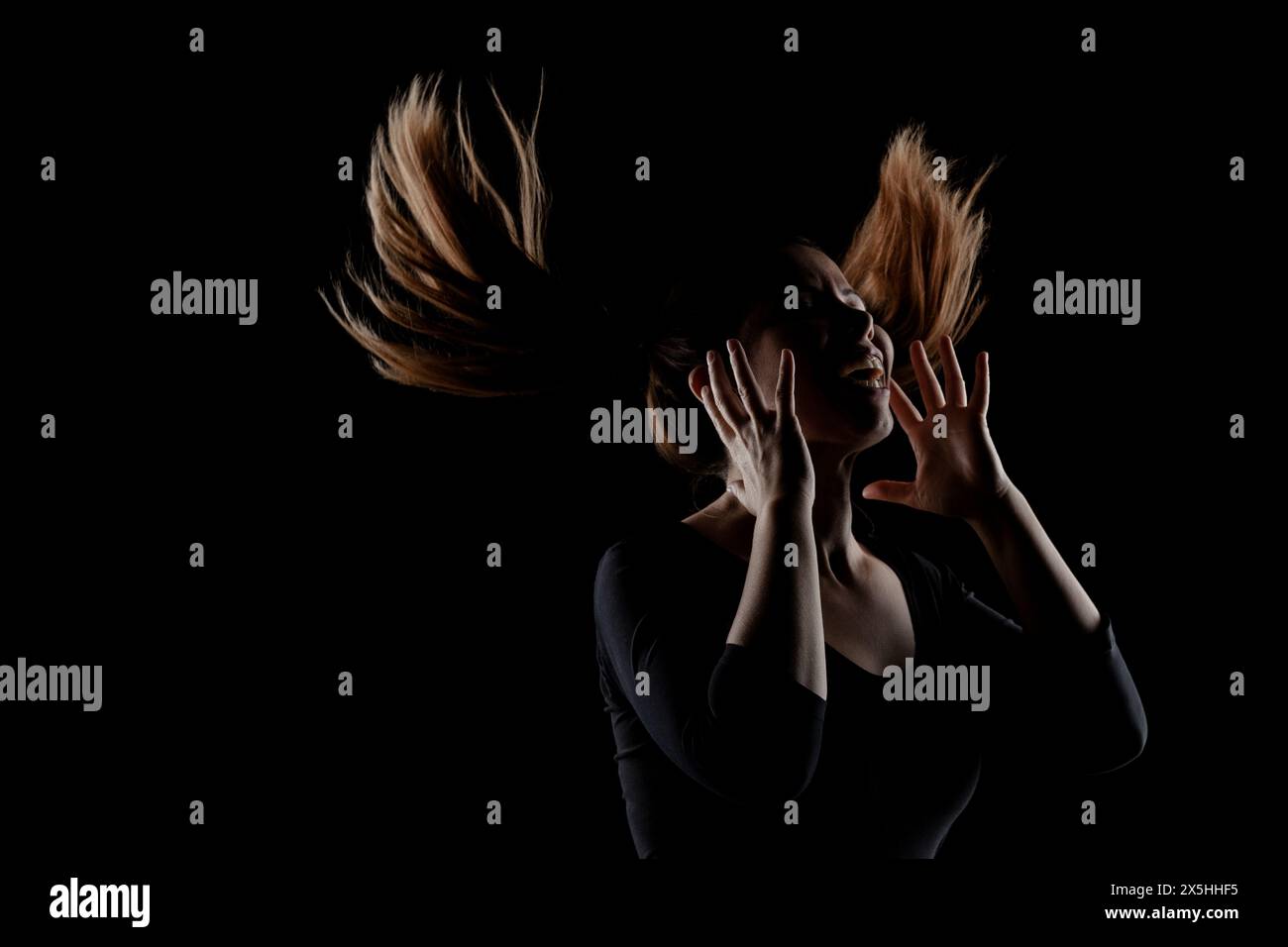Une image frappante d'une femme capturée avec ses cheveux jetés dramatiquement dans l'air, silhouettée sur un fond noir pur, soulignant le mouvement A. Banque D'Images