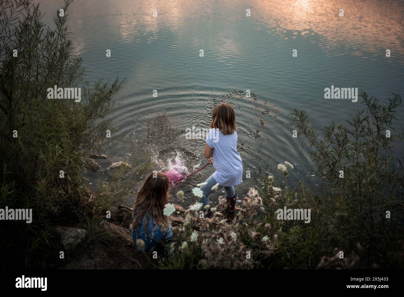 Jeunes enfants éclaboussant de l'eau dans le lac au coucher du soleil Banque D'Images