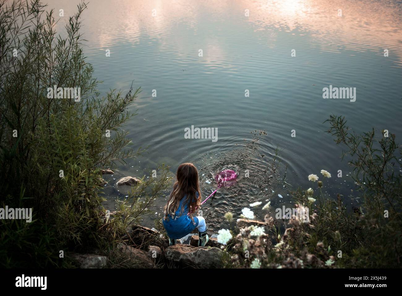Jeune fille éclaboussant de l'eau dans le lac au coucher du soleil Banque D'Images