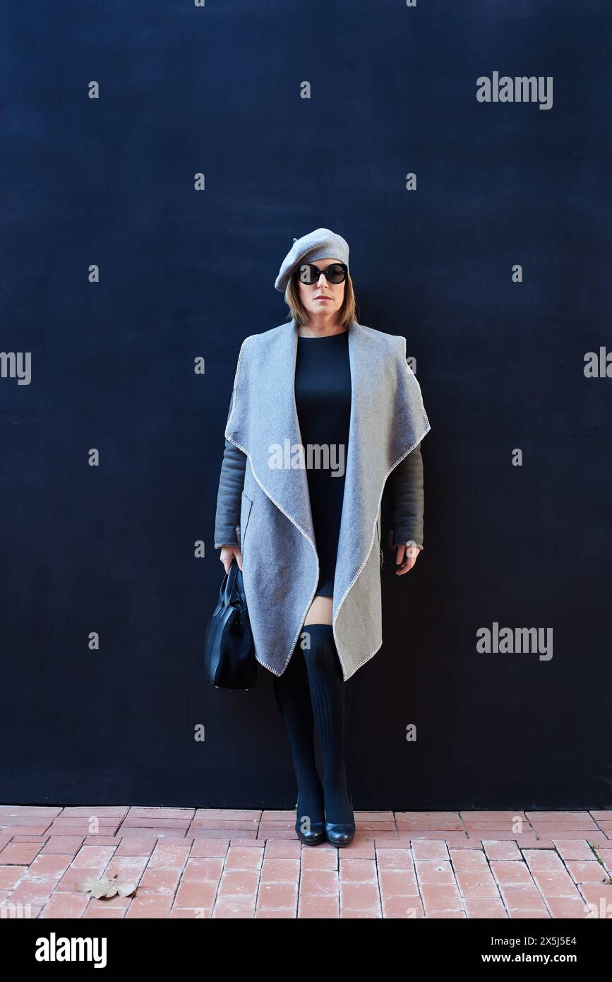 Femme élégante en béret et manteau sur fond sombre Banque D'Images