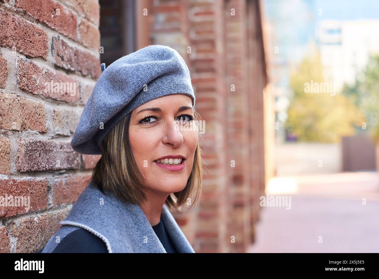 Femme souriante en béret par mur de briques, style décontracté Banque D'Images