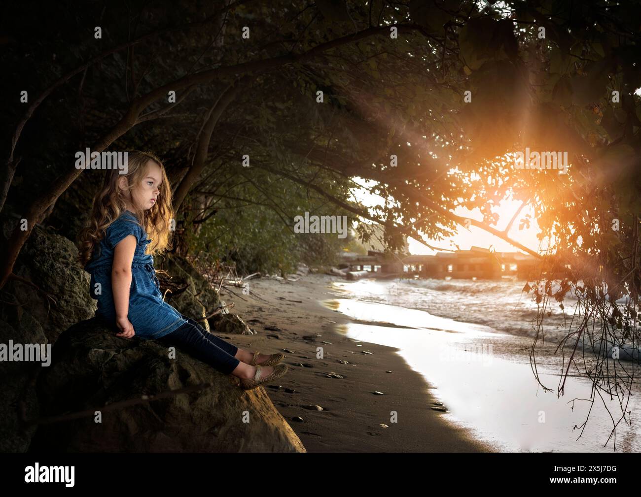 Petite fille avec de longues boucles blondes regardant l'eau sous le ciel ensoleillé Banque D'Images