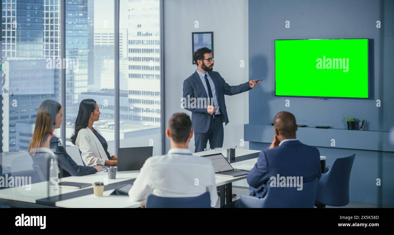 Réunion de salle de conférence de bureau diversifiée : le chef de projet masculin utilise un téléviseur mural à écran vert Chroma Key TV présentant une opportunité pour le groupe d'investisseurs. Stratégie de produit e-commerce. Grand angle moyen Banque D'Images