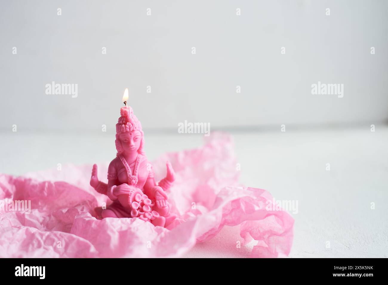 Une bougie rose est placée sur un pétale rose, ressemblant à une fleur délicate. La teinte magenta contraste magnifiquement avec le matériau naturel, créant un stu Banque D'Images