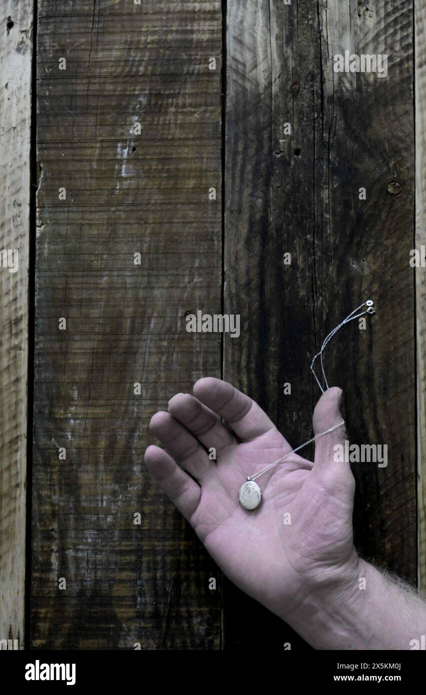 Une main ouverte d'homme posée sur le vieux fond de bois avec médaillon argenté reposant sur la paume, style couverture de livre. Banque D'Images