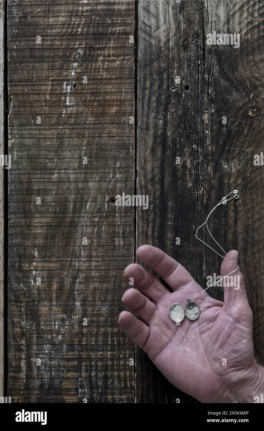 Une main ouverte d'homme posée sur le vieux fond de bois avec médaillon argenté reposant sur la paume, style couverture de livre. Banque D'Images