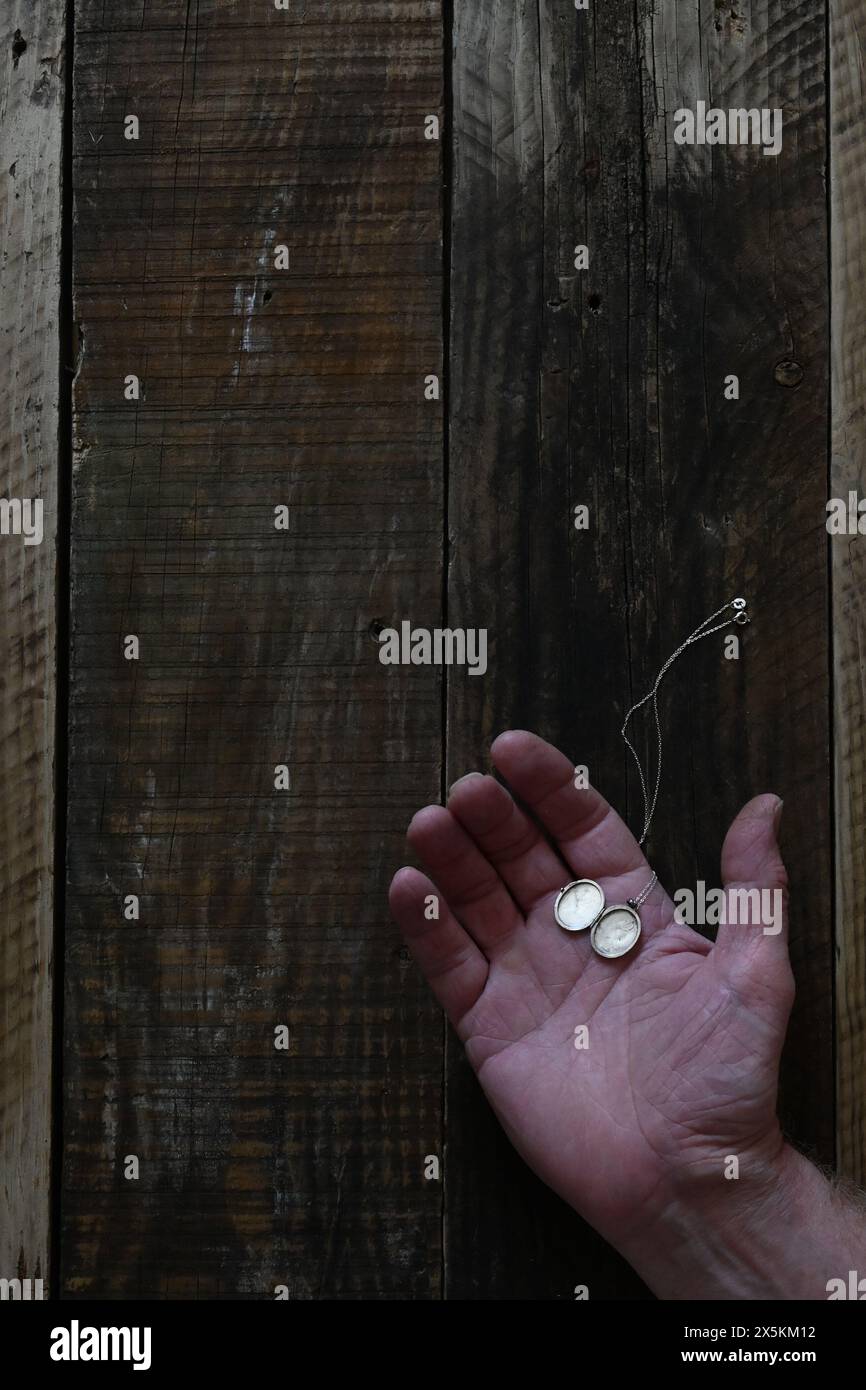 Une main ouverte d'homme posée sur le vieux fond de bois avec médaillon argenté reposant sur la paume, style couverture de livre. Banque D'Images