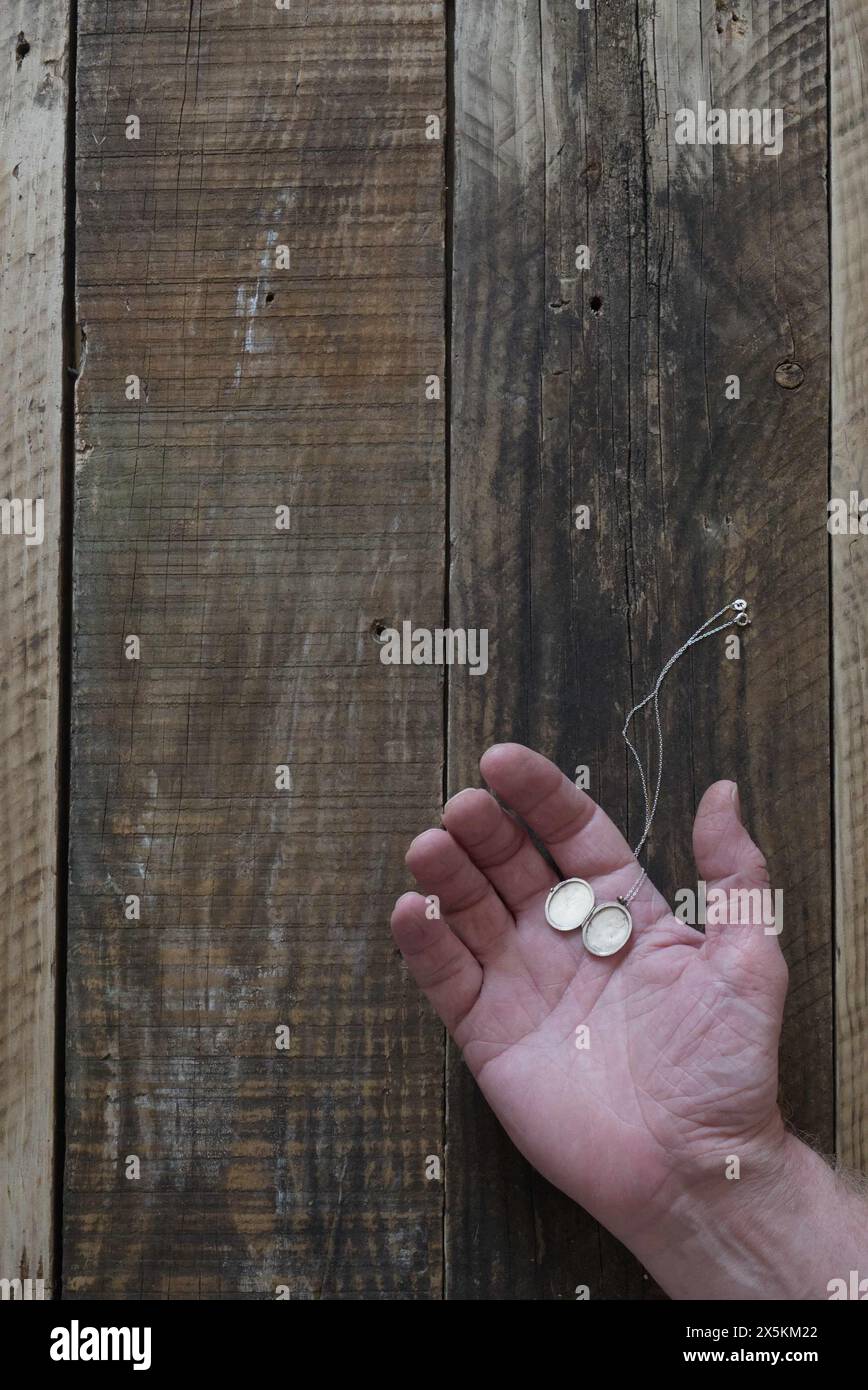 Une main ouverte d'homme posée sur le vieux fond de bois avec médaillon argenté reposant sur la paume, style couverture de livre. Banque D'Images