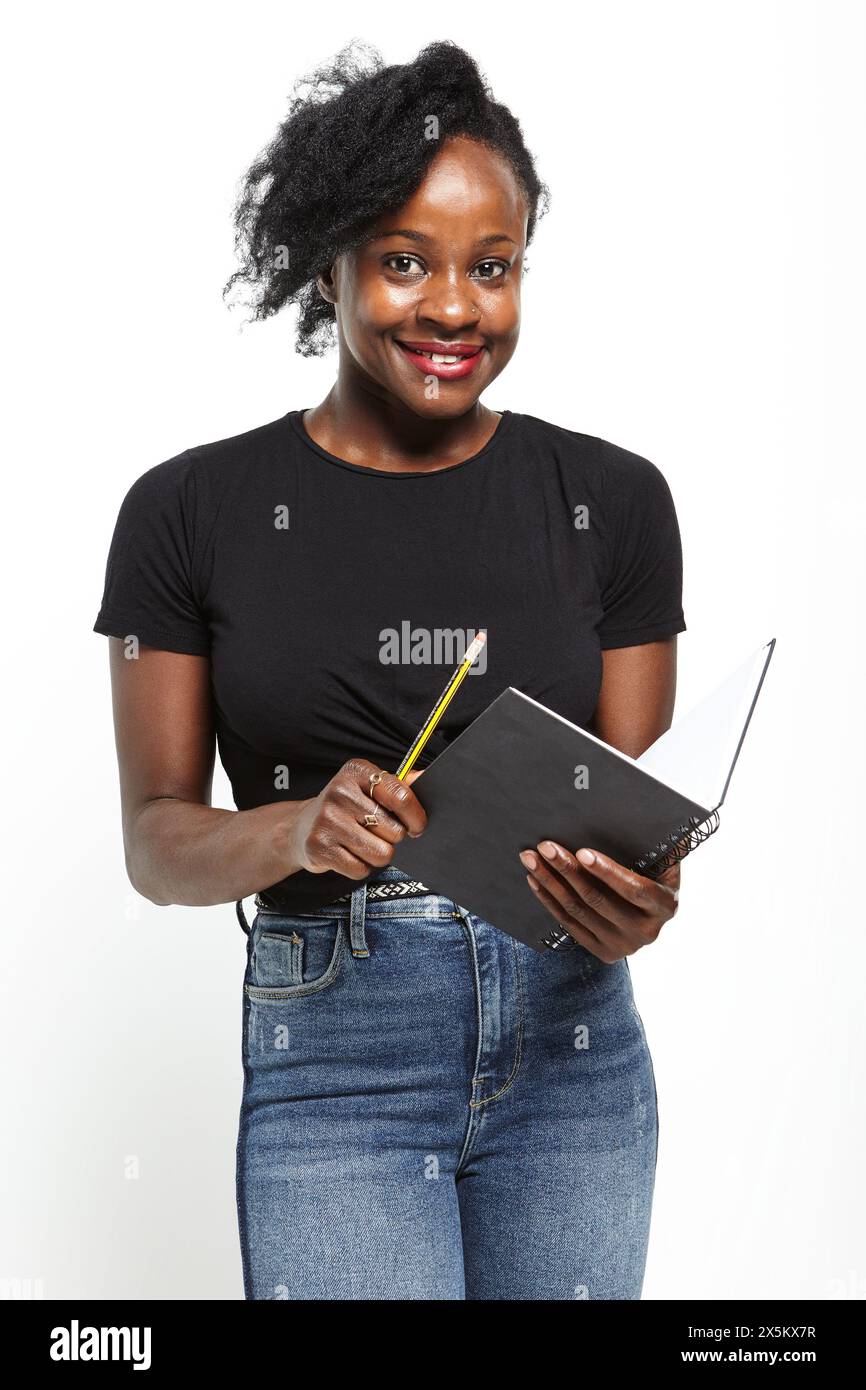 Portrait studio de femme souriante en t-shirt noir et jeans tenant le cahier Banque D'Images