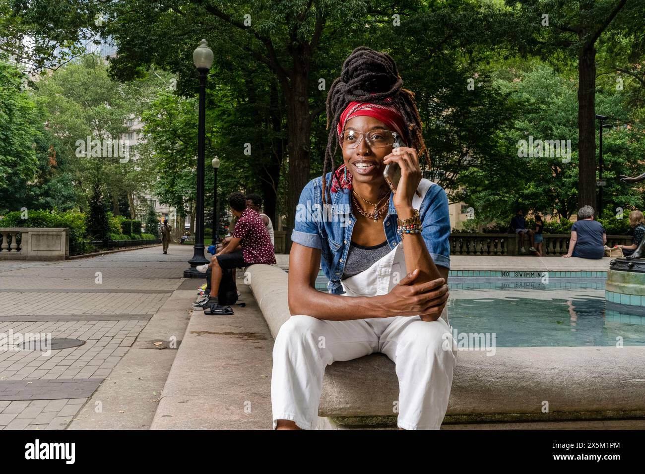 USA, Portrait de jeune femme assise sur le mur dans le parc, parlant sur téléphone intelligent Banque D'Images