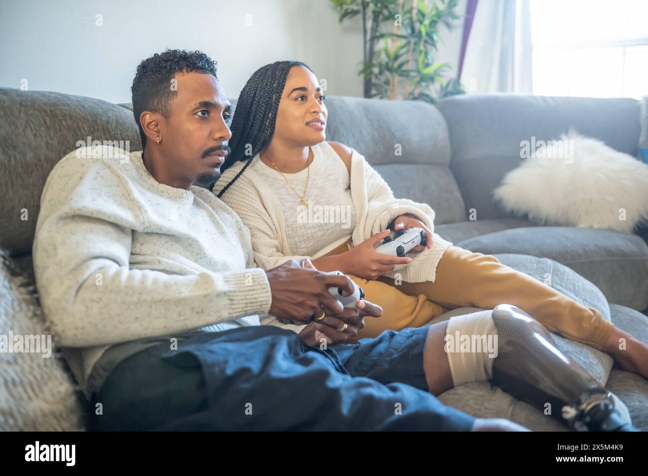 Femme et homme avec la jambe prothétique jouant au jeu vidéo sur le canapé Banque D'Images