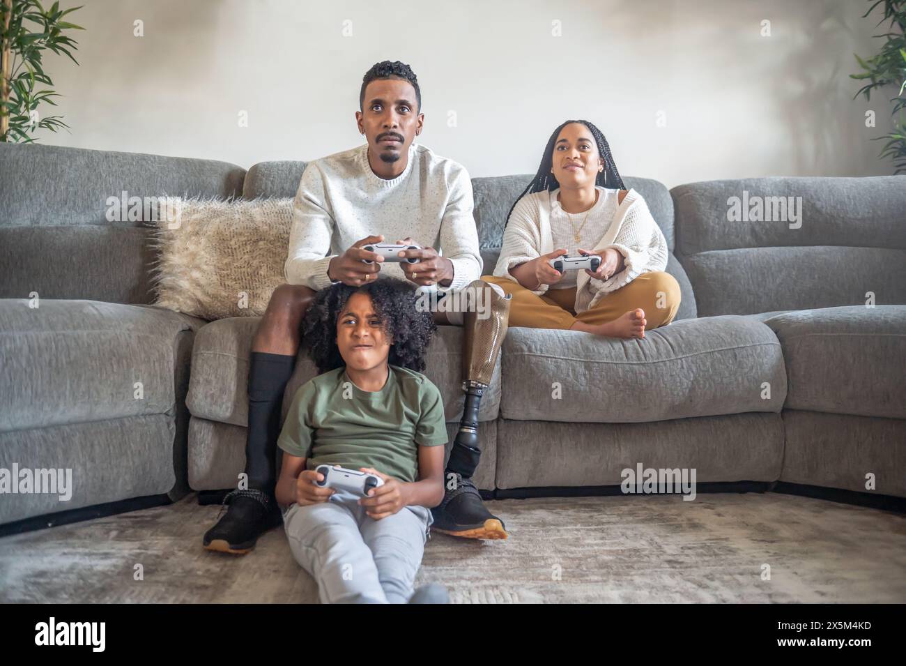 Garçon avec mère et père avec jambe prothétique jouant au jeu vidéo sur le canapé Banque D'Images