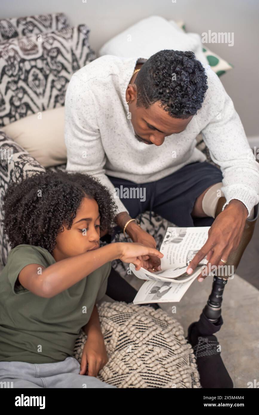 Homme avec un livre de lecture de jambe prothétique avec son fils sur le canapé Banque D'Images