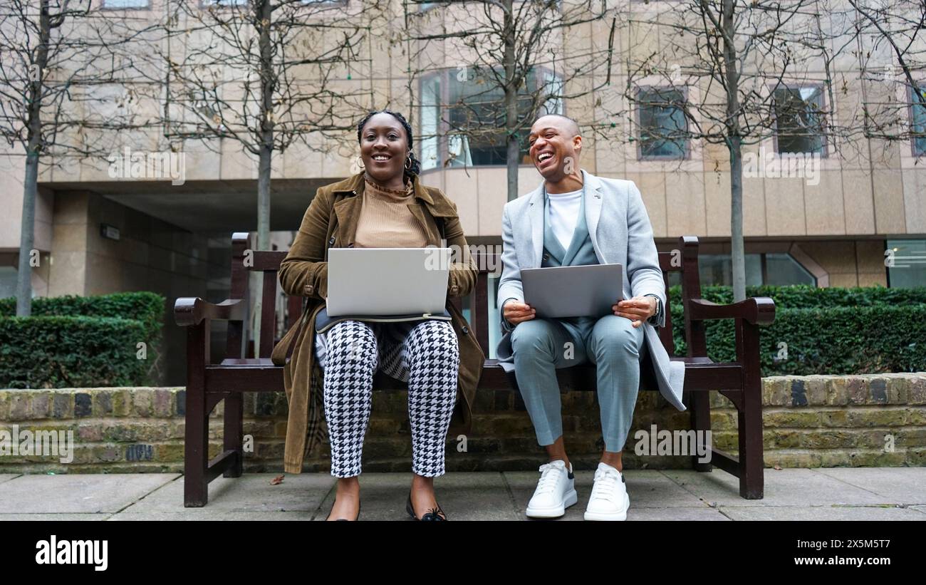 Homme d'affaires et femme assis sur le banc à l'aide d'ordinateurs portables Banque D'Images
