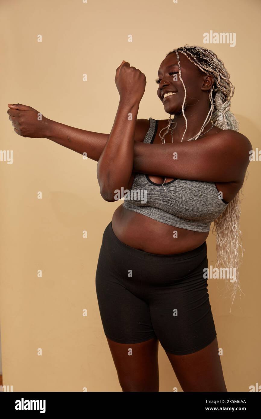 Photo studio d'une femme souriante de taille plus dans des vêtements de sport étirant le bras Banque D'Images