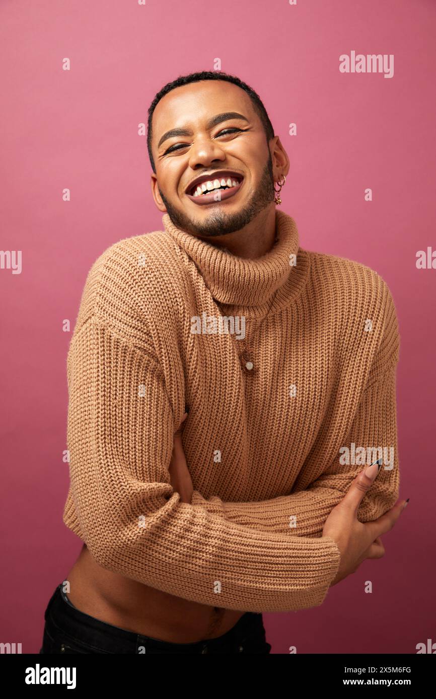 Portrait de studio d'homme queer souriant sur fond violet Banque D'Images