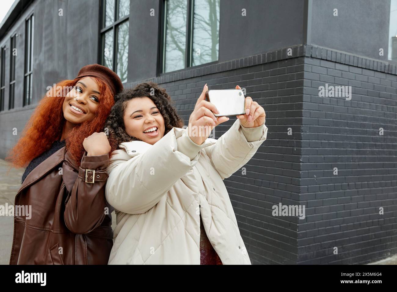 Des femmes souriantes prenant selfie devant un bâtiment noir Banque D'Images