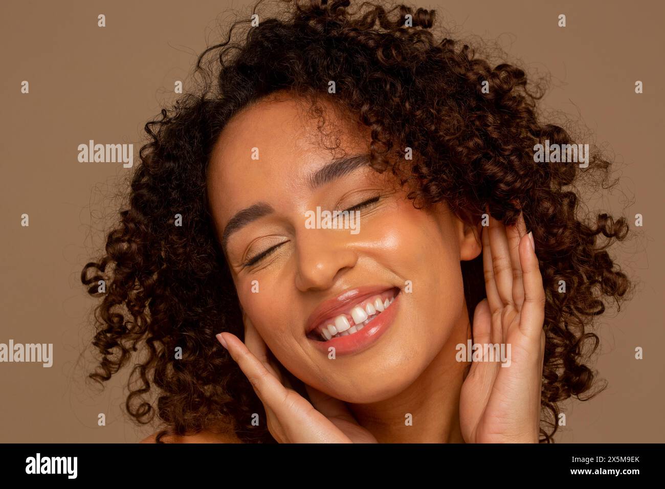 Gros plan d'une femme souriante avec les cheveux bouclés et les yeux fermés Banque D'Images