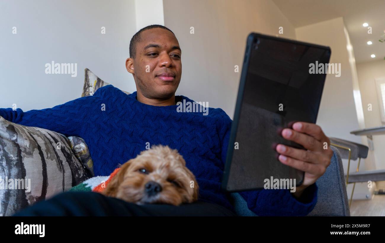 Homme utilisant une tablette, chien reposant sur ses genoux Banque D'Images