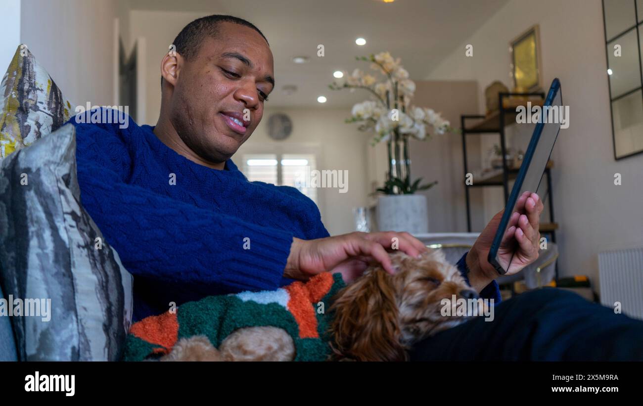 Homme utilisant une tablette, chien reposant sur ses genoux Banque D'Images