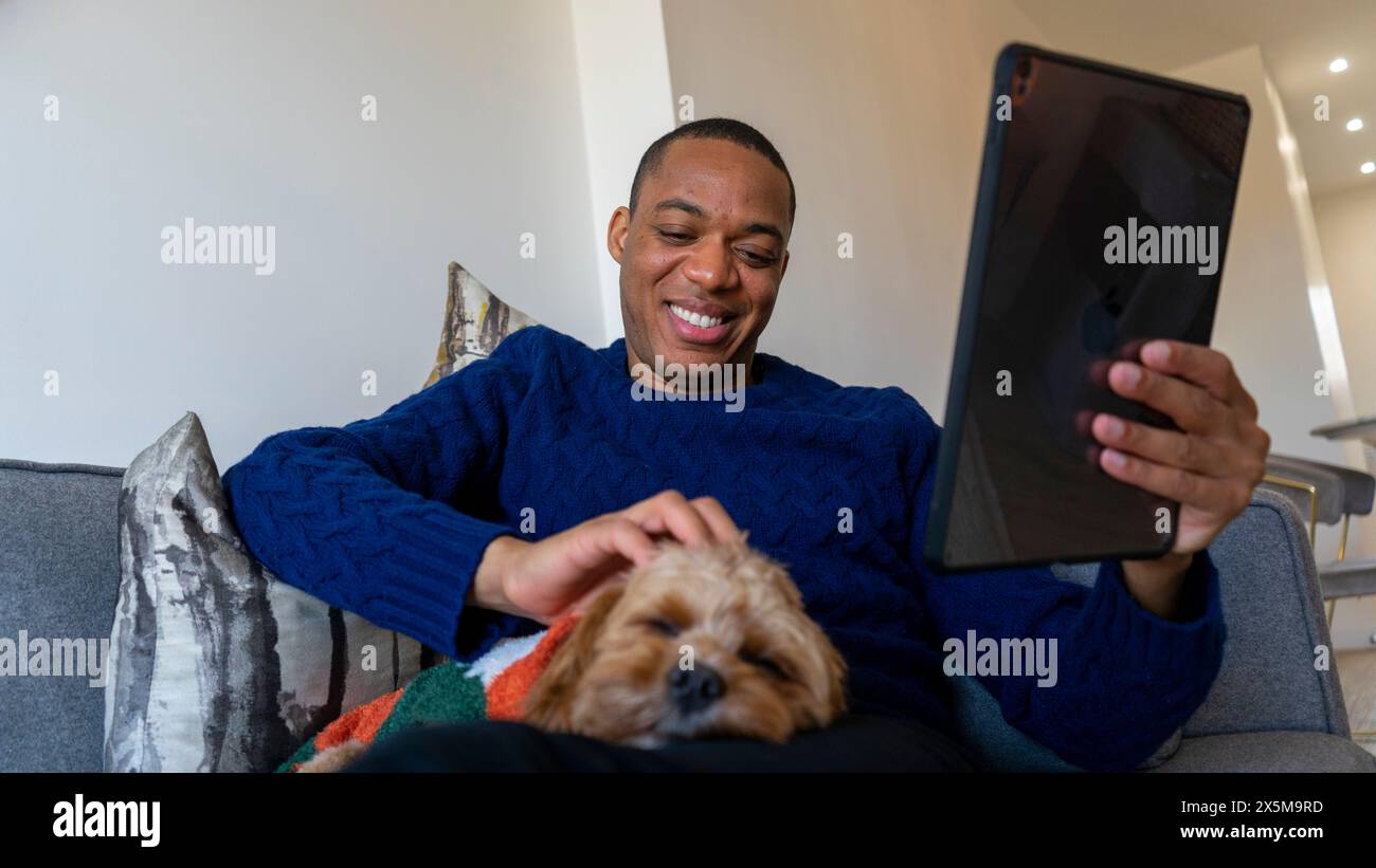 Homme utilisant une tablette, chien reposant sur ses genoux Banque D'Images
