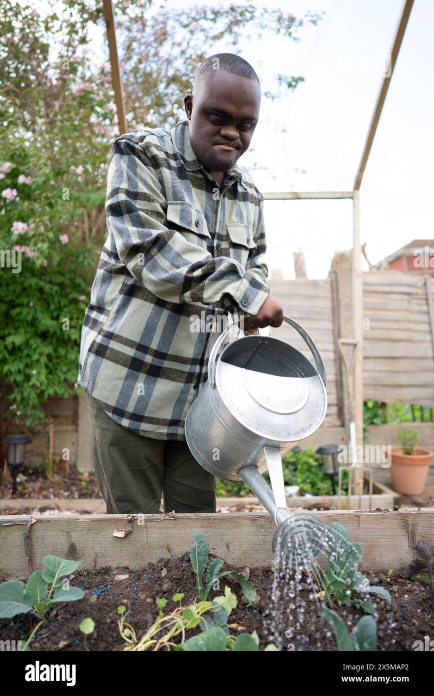 Homme avec le syndrome de Down arrosant les plantes dans le jardin Banque D'Images