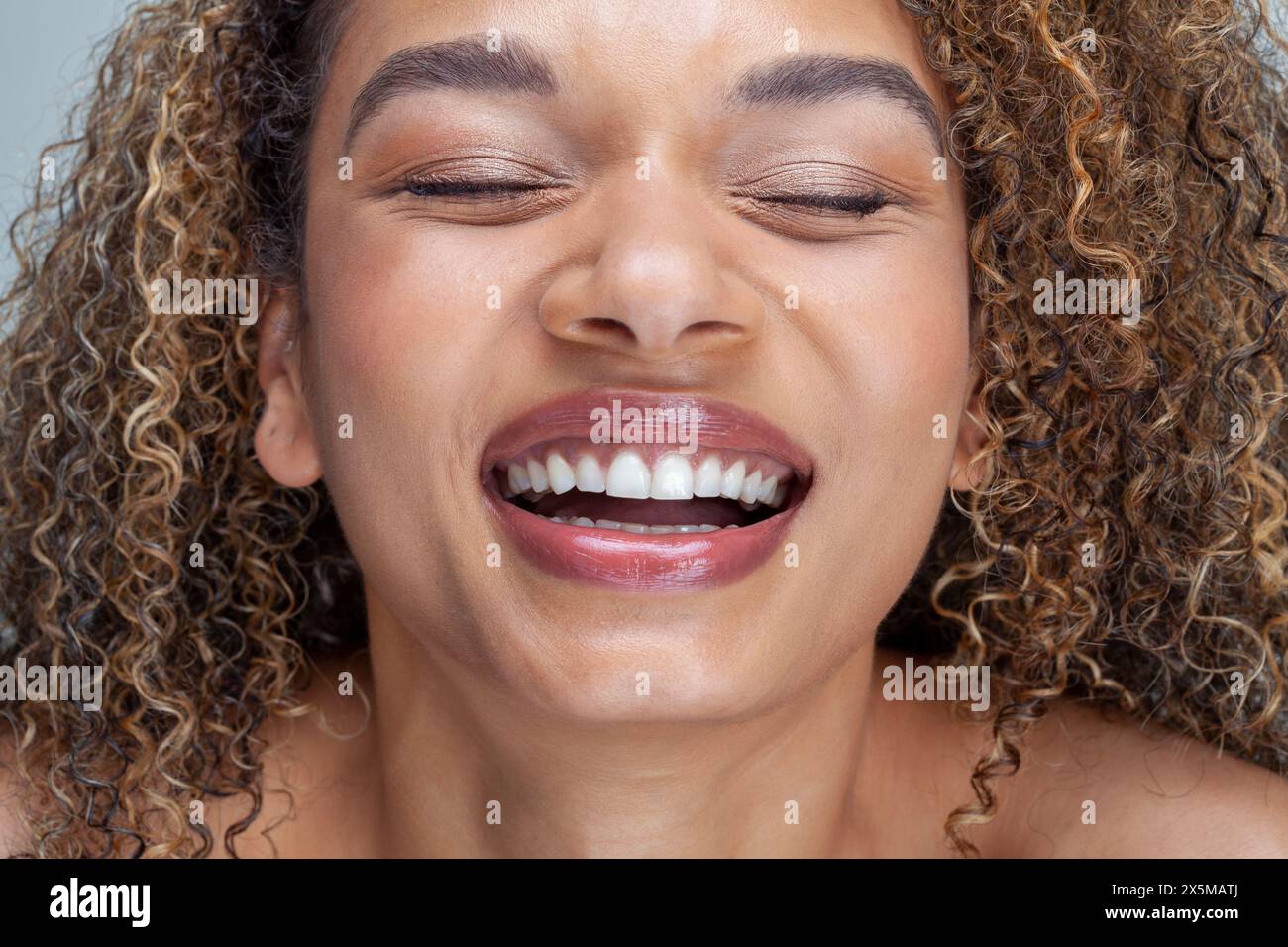 Gros plan d'une femme souriante avec les cheveux bouclés et les yeux fermés Banque D'Images