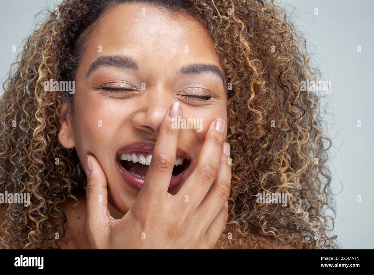 Gros plan d'une femme souriante avec les cheveux bouclés et les yeux fermés Banque D'Images