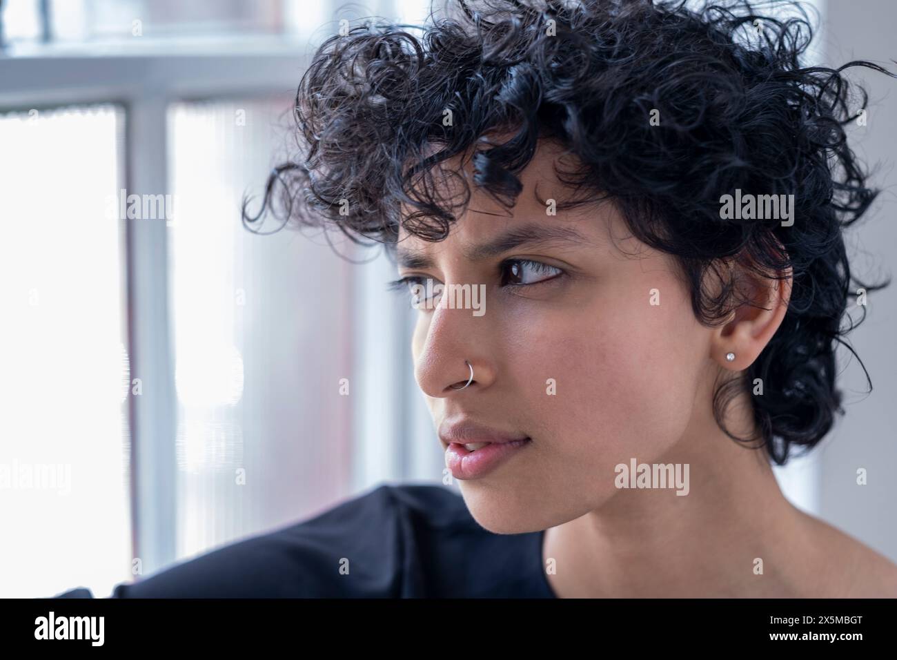Jeune femme aux cheveux bouclés regardant par la fenêtre Banque D'Images