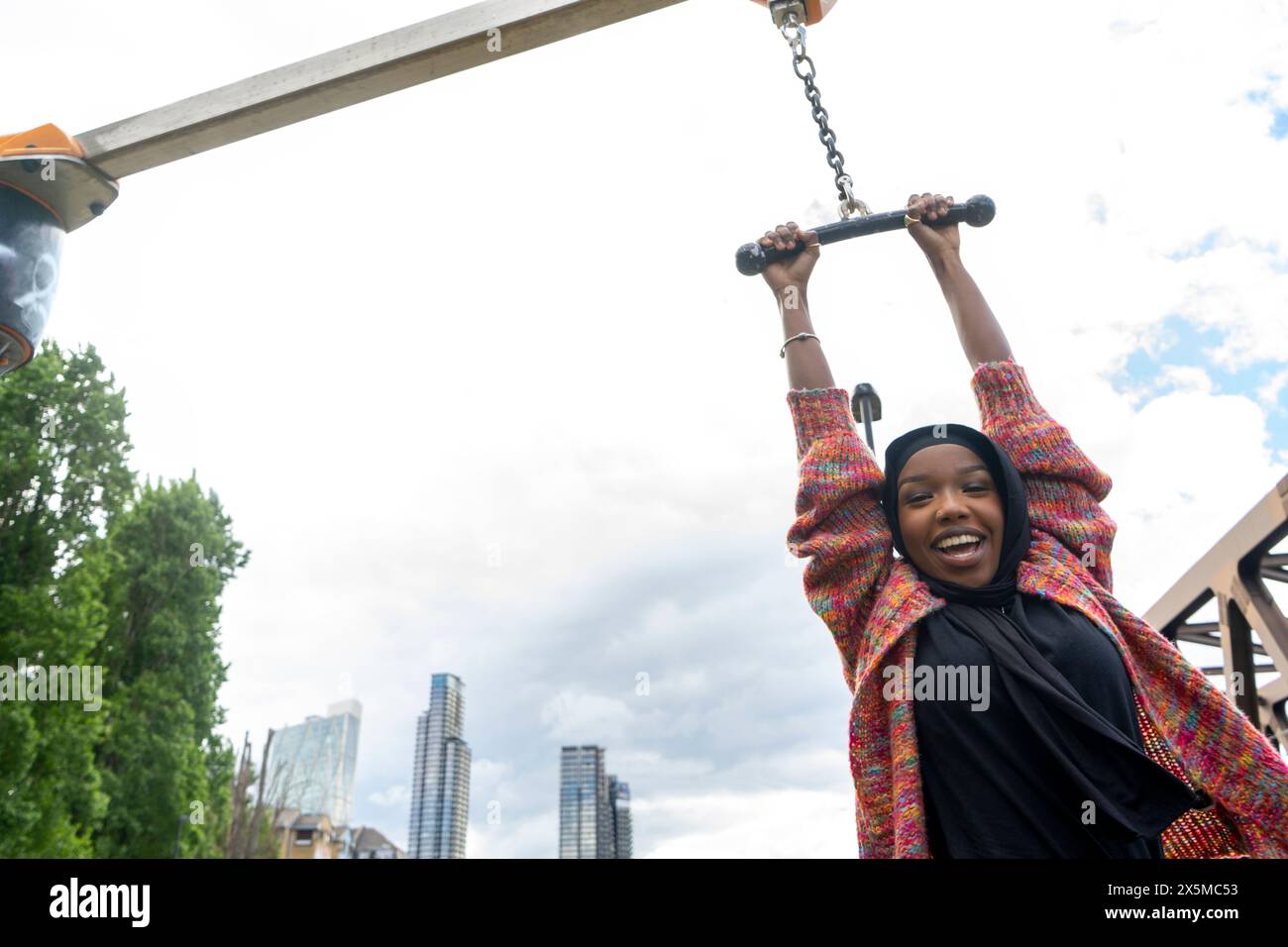 Portrait d'une femme souriante portant le hijab accroché à la machine d'exercice dans le parc Banque D'Images