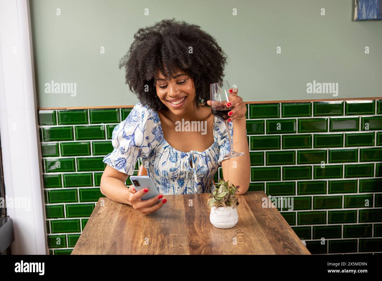 Royaume-Uni, Londres, femme souriante avec verre de vin rouge et téléphone intelligent à la table de café Banque D'Images