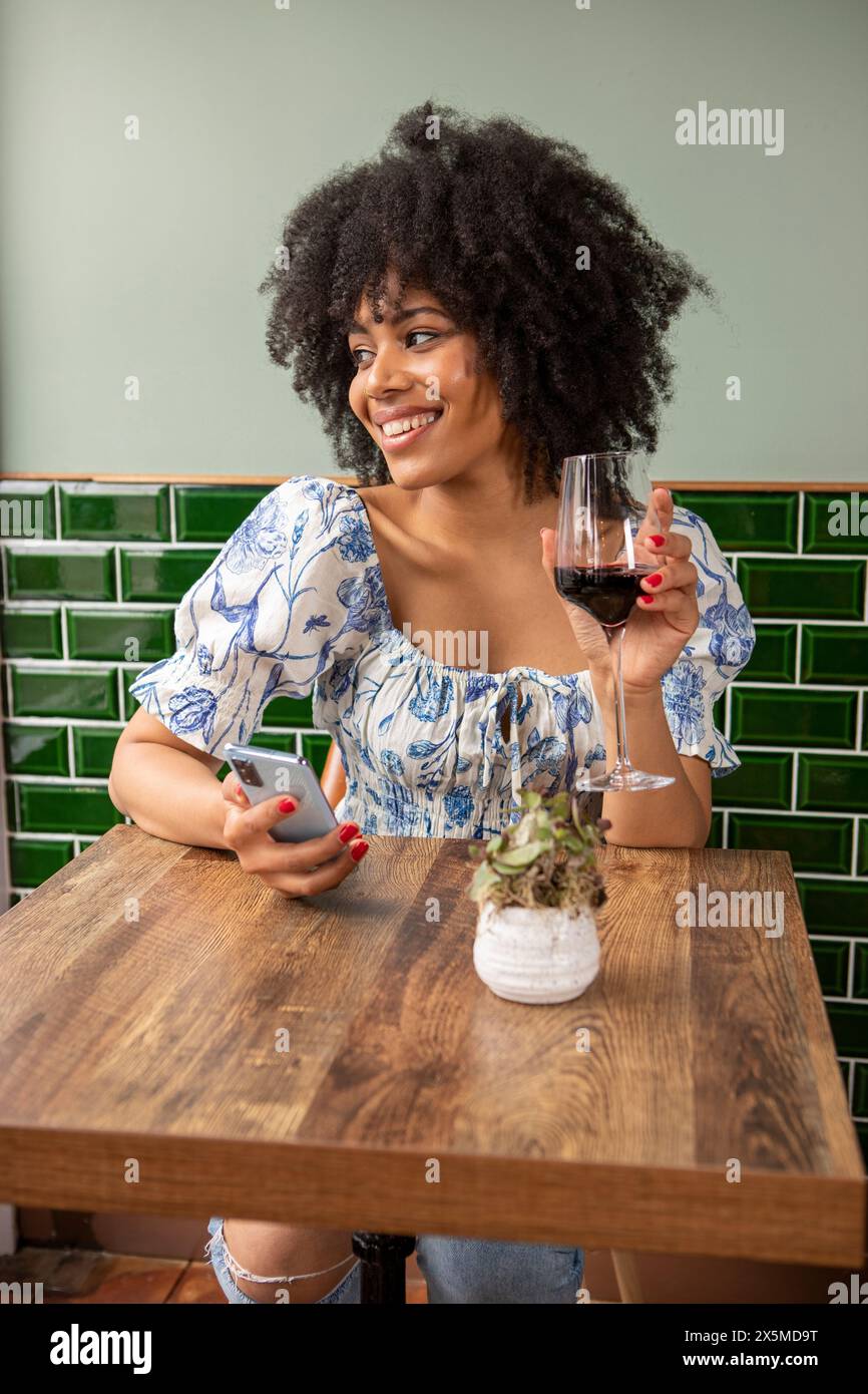 Royaume-Uni, Londres, femme souriante avec verre de vin rouge et téléphone intelligent à la table de café Banque D'Images