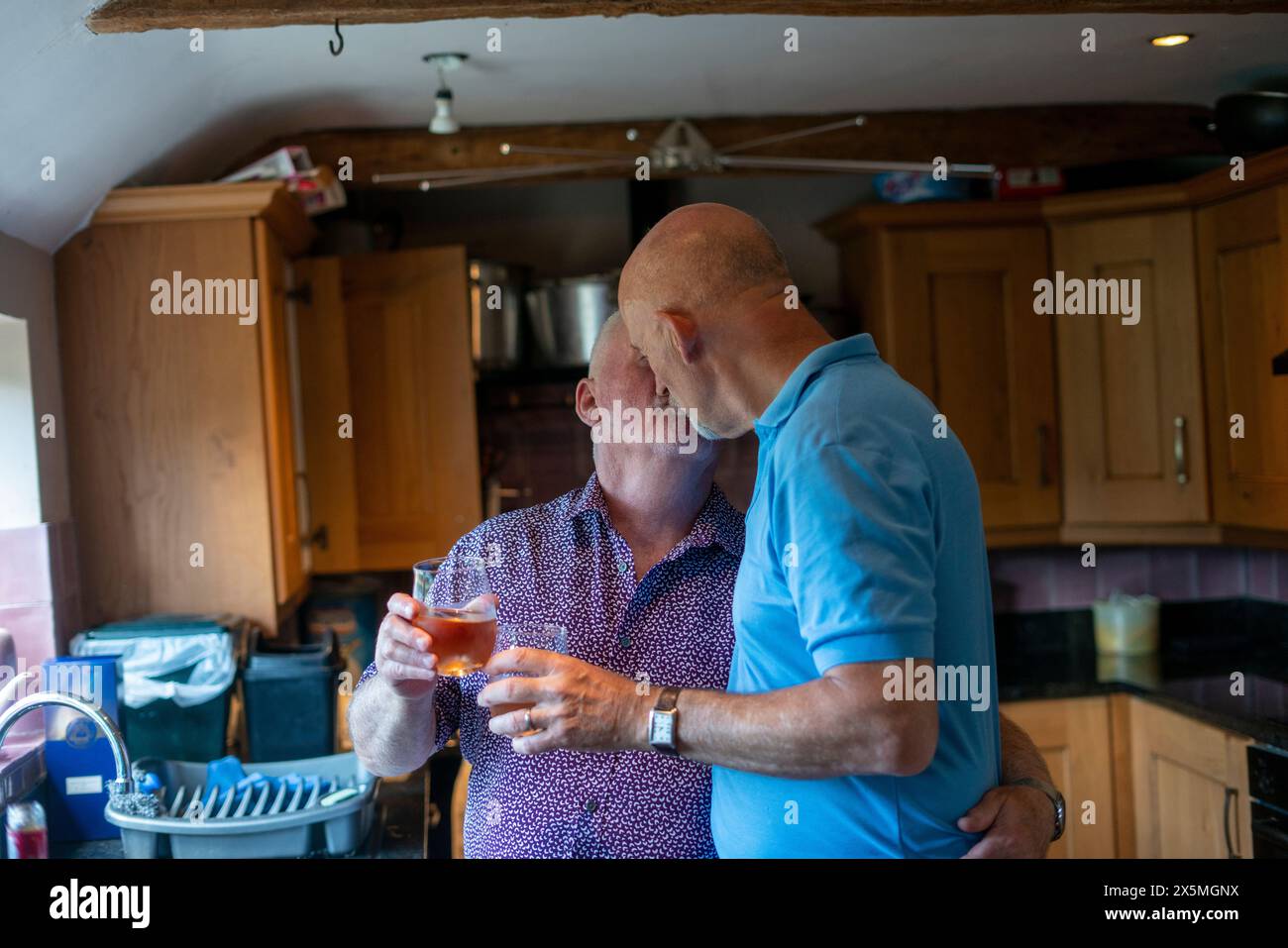 Couple masculin senior élevant des toasts et s'embrassant dans la cuisine Banque D'Images