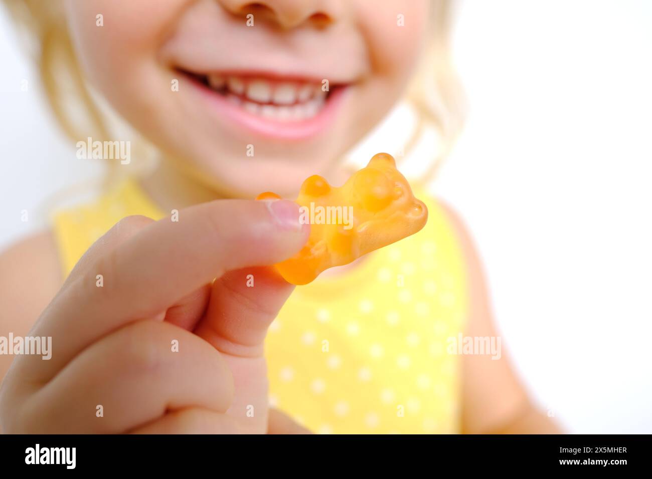 petit enfant joyeux tient des bonbons, fille blonde de 3 ans veut manger des bonbons gélatineux avec le sourire, ours gommé, enfant a bon appétit, enfance heureuse, Banque D'Images