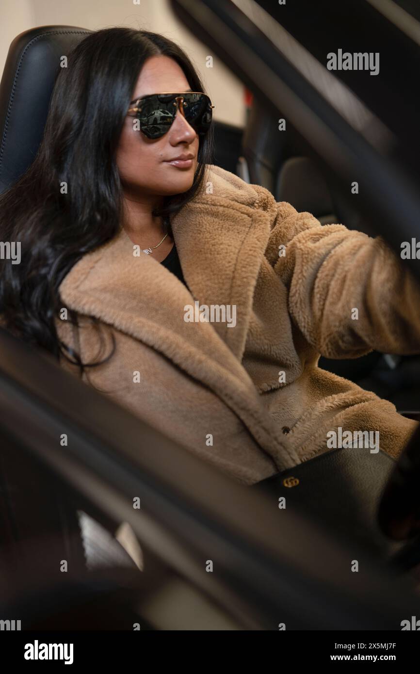 Jeune femme en lunettes de soleil assise dans une voiture de luxe Banque D'Images