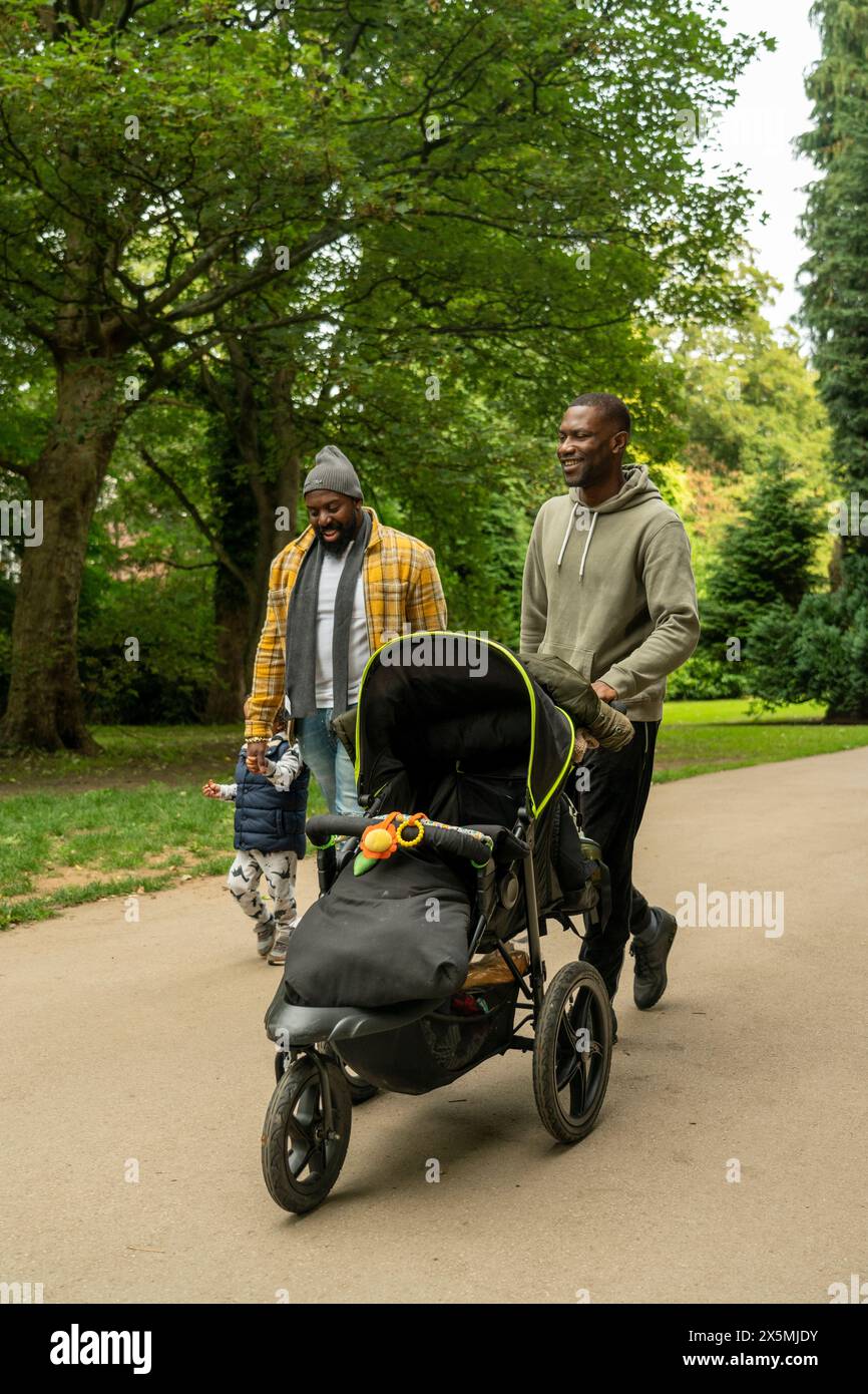 Deux hommes avec fille et poussette de bébé marchant dans le parc Banque D'Images