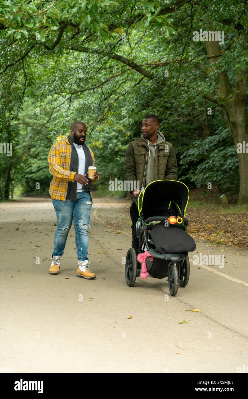 Deux hommes avec fille et poussette de bébé marchant dans le parc Banque D'Images