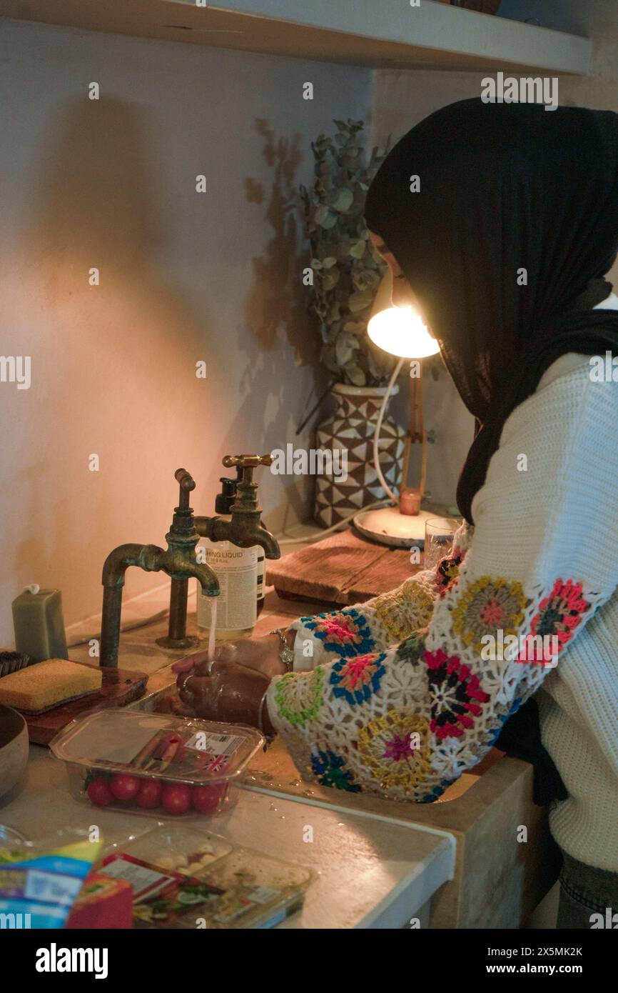 Femme portant le hijab lavant les tomates cerises dans l'évier de cuisine Banque D'Images