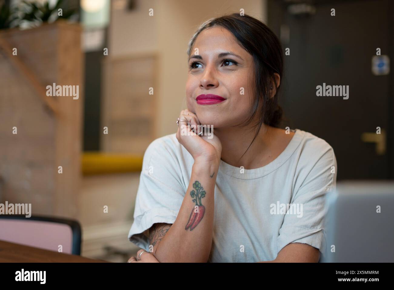 Femme souriante assise dans le bureau avec la main sur le menton Banque D'Images