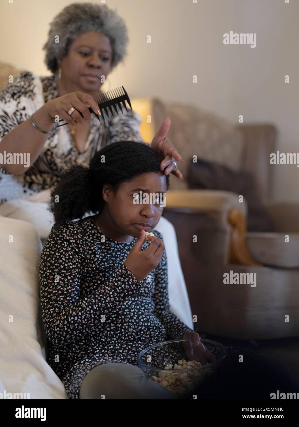 Mère coiffant ses filles en regardant la télé Banque D'Images