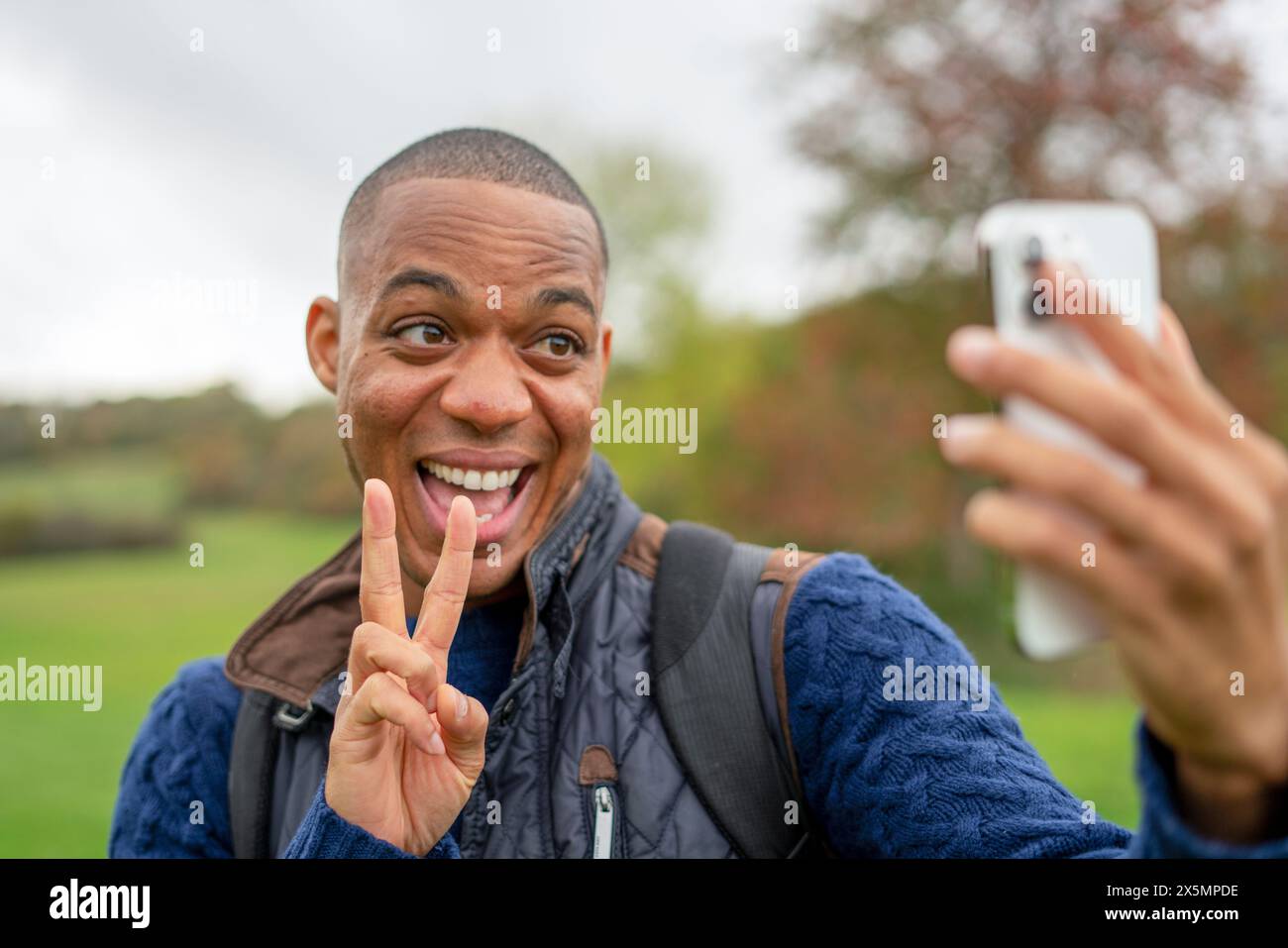 Homme souriant faisant un geste de paix et prenant selfie Banque D'Images