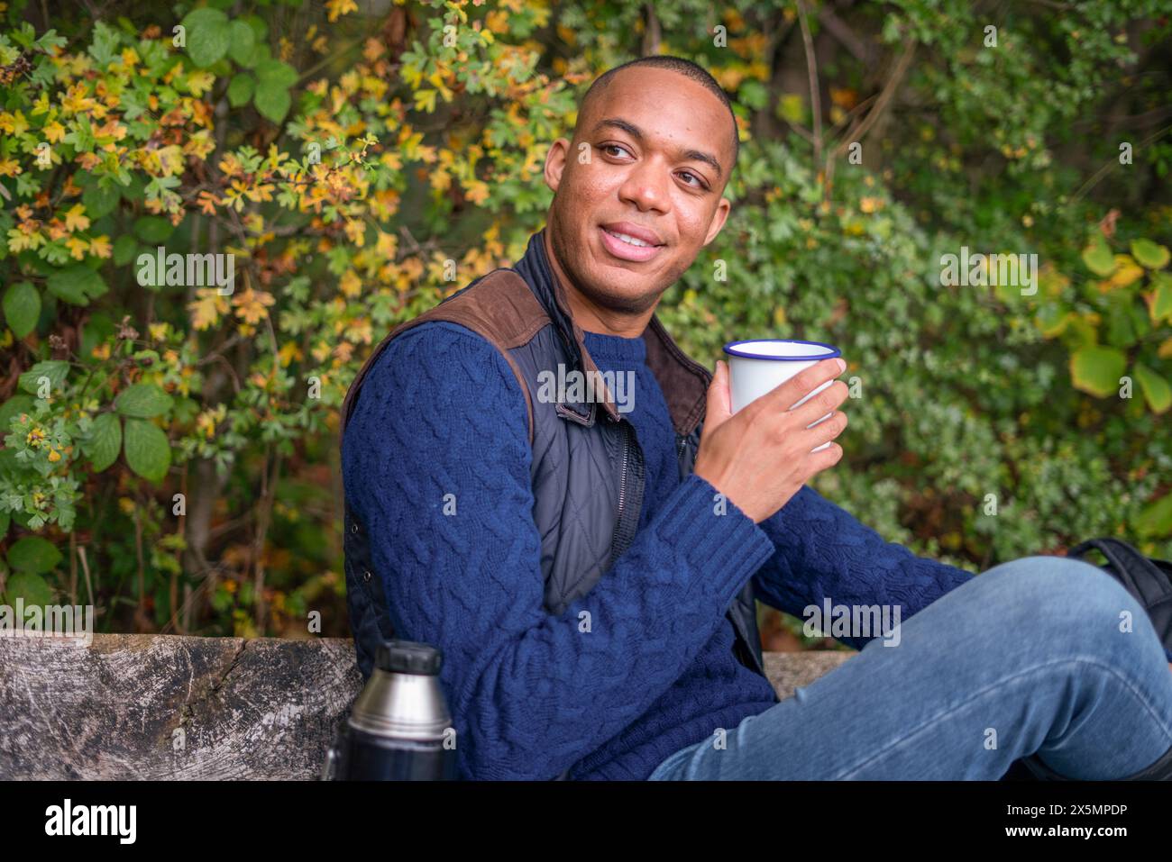 Homme tenant une tasse en métal et assis sur le banc Banque D'Images