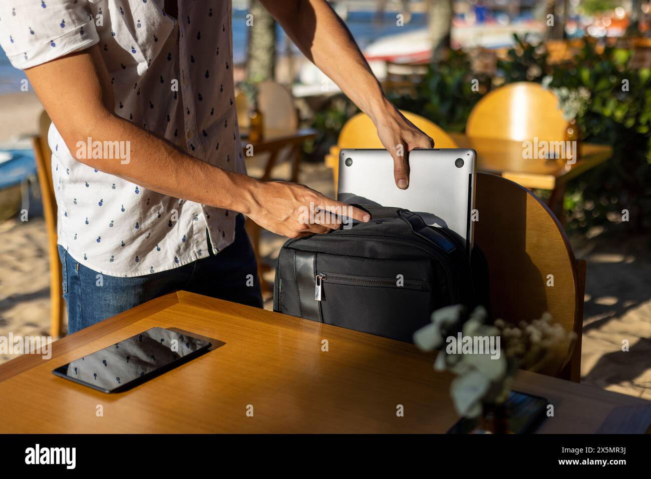 Homme mettant des appareils mobiles dans un sac à dos à la table de café de plage Banque D'Images