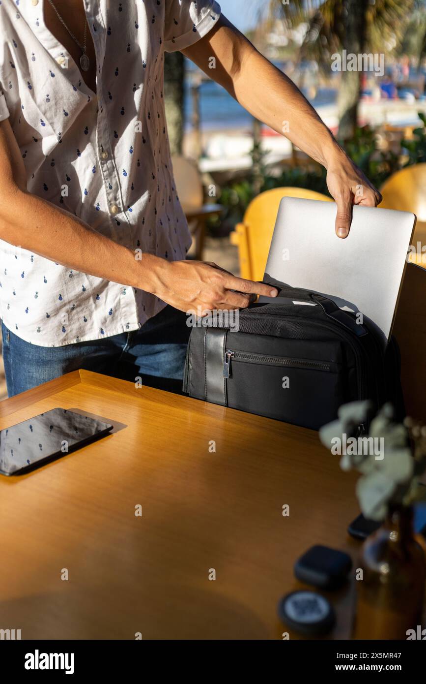 Homme mettant des appareils mobiles dans un sac à dos à la table de café de plage Banque D'Images