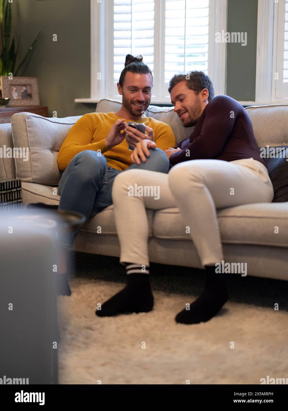 Couple gay regardant le téléphone tout en se relaxant sur le canapé à la maison Banque D'Images