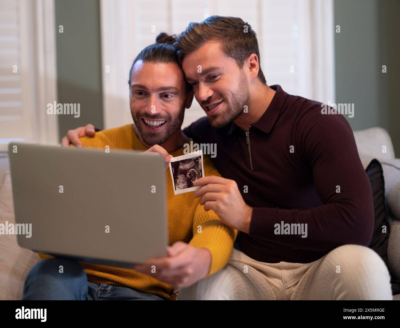 Couple gay montrant l'échographie d'un bébé lors d'un appel vidéo à la maison Banque D'Images