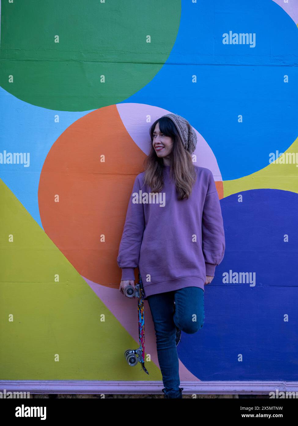 Portrait de femme debout avec skateboard contre mur multicolore Banque D'Images